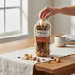 Mellow Monkey dark chocolate almond caramel popcorn in a clear bag held by a hand on a wooden table with a mug