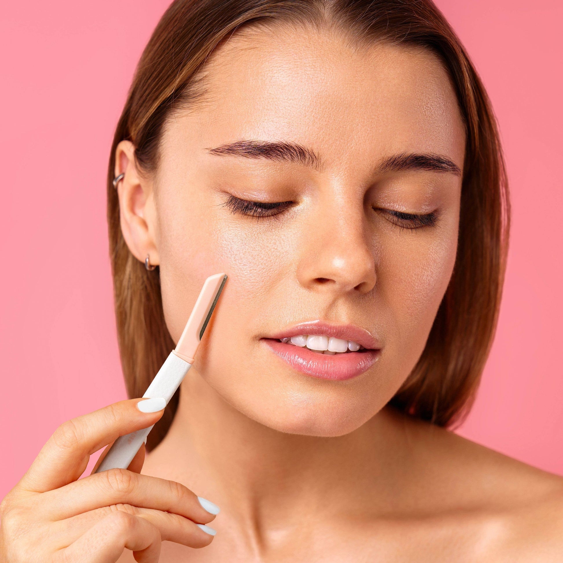 Mellow Monkey Fuzz Off Dermaplaner Facial Razor in pink and white, used by a woman on her cheek for smooth skin.