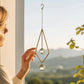Mellow Monkey diamond-shaped celestial suncatcher with gold chains and hanging crystals held by a woman near a window