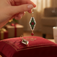 Mellow Monkey diamond-shaped earrings featuring holly leaves and red berries on a red velvet cushion by a Christmas tree
