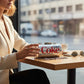 Woman holding a Mellow Monkey metallic silver Diet Coke can novelty bag with a chain strap at a cafe table.