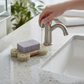 Mellow Monkey dog bone shaped bioplastic soap lift pad holding a bar of soap on a bathroom vanity counter