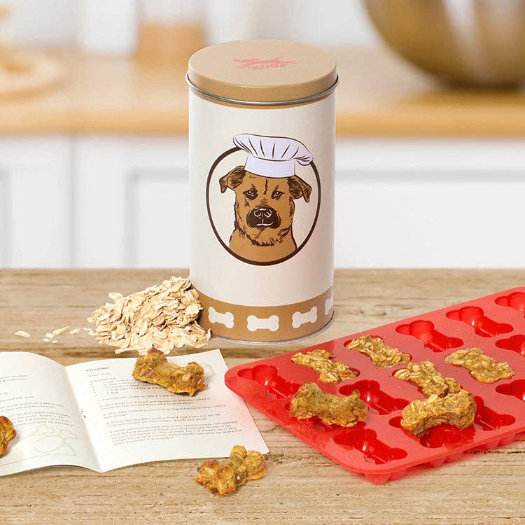 Mellow Monkey Kobe dog treat kit with a keepsake tin, red silicone bone mold, and recipe book on a wooden table.