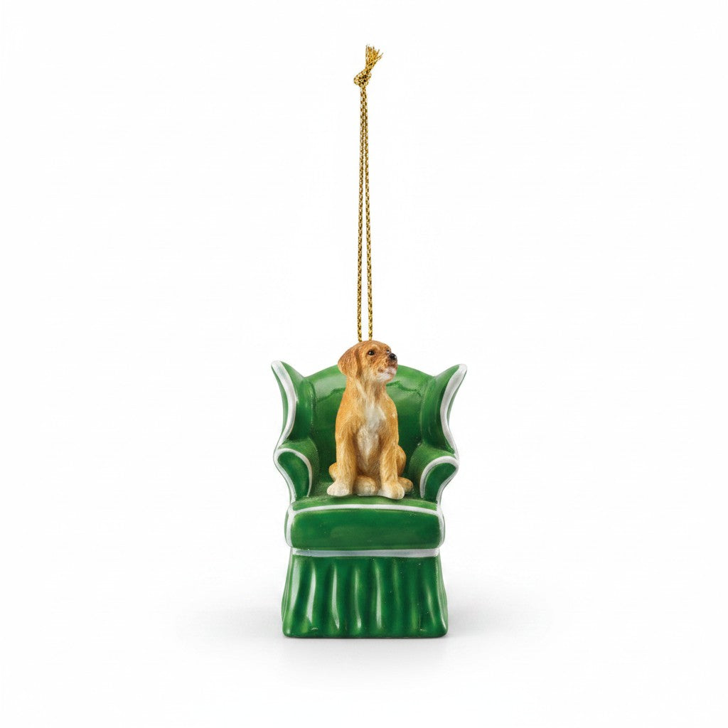 Mellow Monkey resin dog ornament sitting in a green wingback chair with a gold hanging cord on a white background