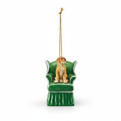 Mellow Monkey resin dog ornament sitting in a green wingback chair with a gold hanging cord on a white background