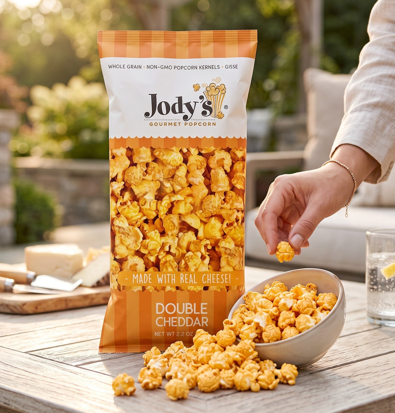 Mellow Monkey Jody's Double Cheddar popcorn in a clear bag with a bowl of cheesy popcorn on an outdoor table