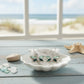 Mellow Monkey mint and green dragonfly earrings in a white shell dish on a beach-themed table.