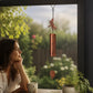Mellow Monkey dragonfly wind bell with a mellow patina finish hanging by a window with a woman looking outside.