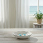 Mellow Monkey dusky blue faceted crystal teardrop earrings resting in a small white ceramic dish by a beach window.