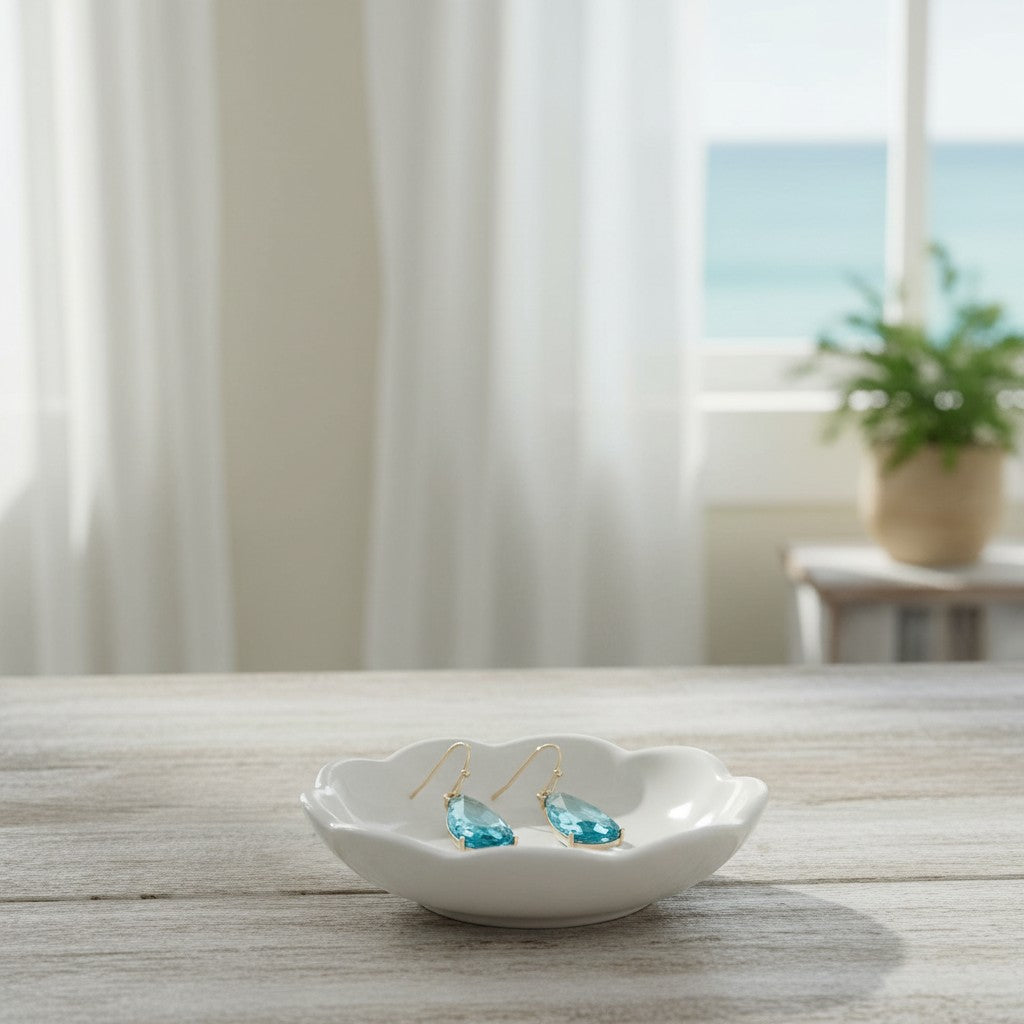 Mellow Monkey dusky blue faceted crystal teardrop earrings resting in a small white ceramic dish by a beach window.