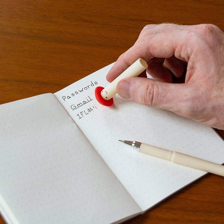 Mellow Monkey erasable mushroom pen being used to erase text in a notebook on a wooden desk.