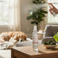 Mellow Monkey Evergreen Forest pet house room spray bottle being used in a cozy living room with a dog in the background