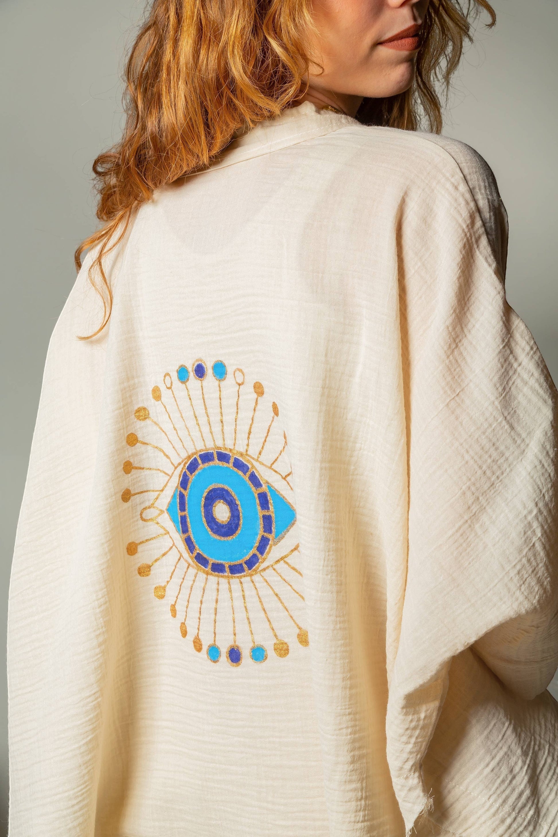 Mellow Monkey cream 4-layer muslin kimono robe with hand-painted blue and gold evil eye design on back.