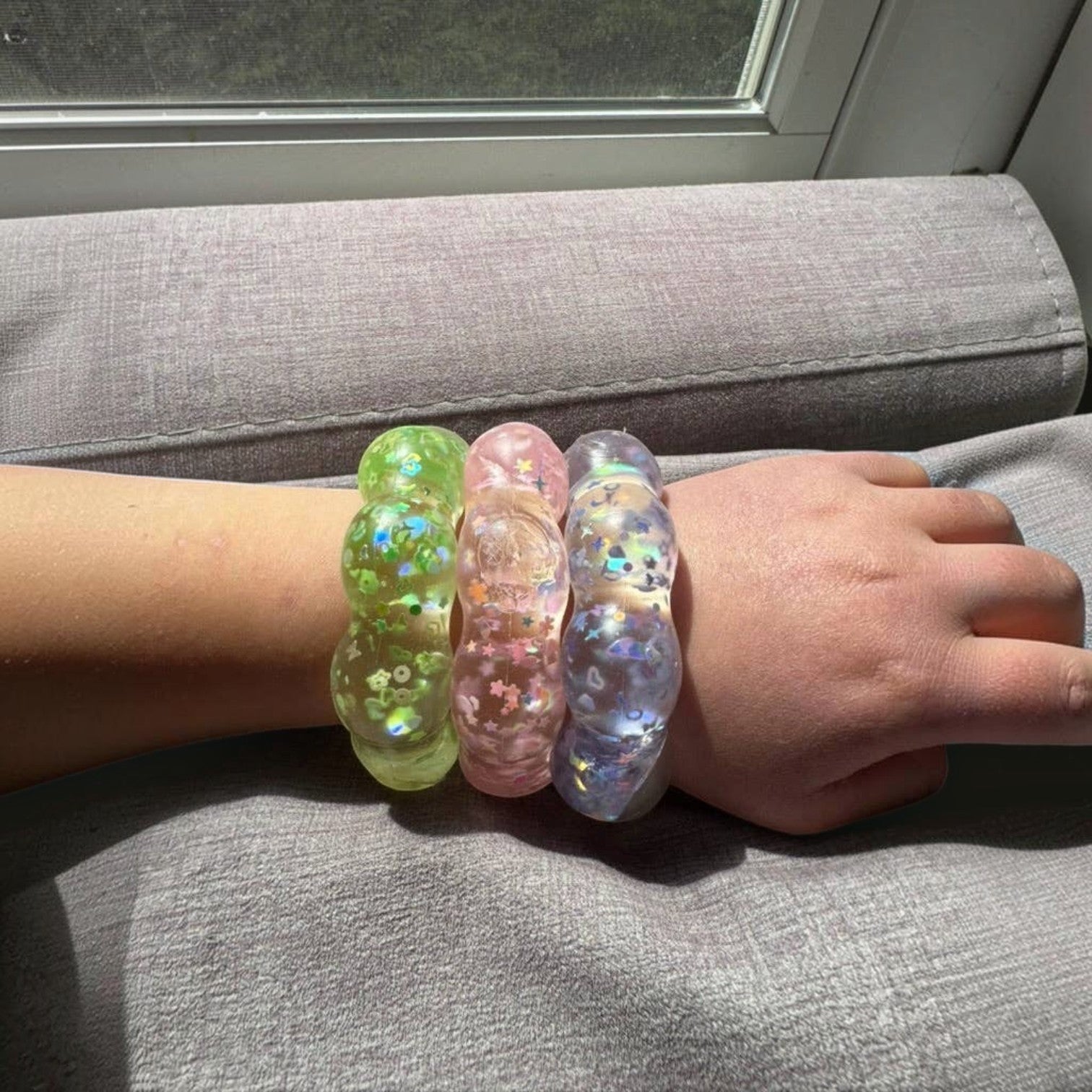 Mellow Monkey Feelzies sensory bracelets in lime, pink, and clear with glitter, worn on a wrist for stress relief.