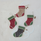 Mellow Monkey felt stocking ornaments in red, green, and tan with pinecone and bead accents on a white background