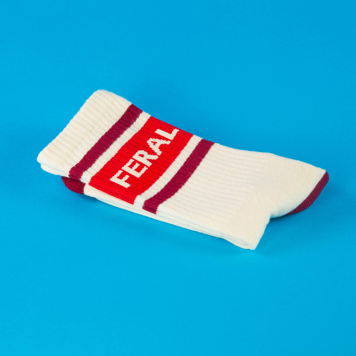 Mellow Monkey Feral gym crew socks in off-white with maroon stripes and text on a bright blue background.