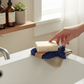 Mellow Monkey royal blue fish-shaped bioplastic soap lift pad under a bar of soap on a bathroom sink