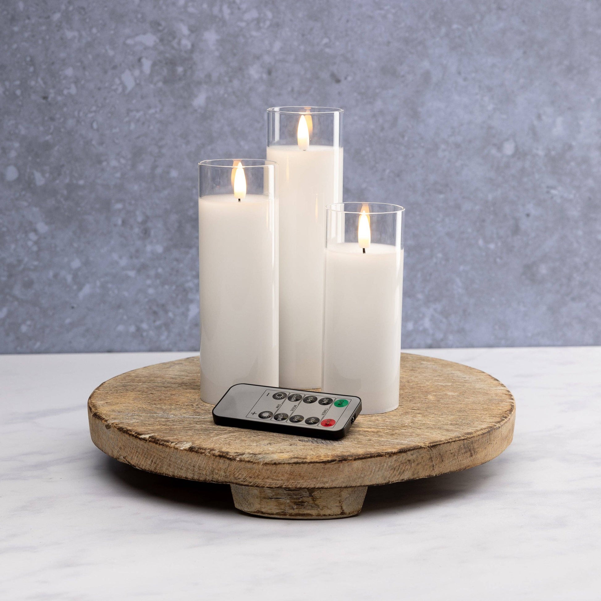 Mellow Monkey set of three white flameless LED pillar candles in glass sleeves with a remote control on a wood tray.