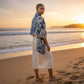 Mellow Monkey double-sided floral shawl with eyelash fringe, draped over a woman on a beach at sunset.