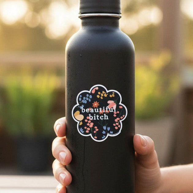 Mellow Monkey floral vinyl sticker with empowering text on a matte black water bottle held by a hand outdoors.
