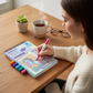 Mellow Monkey Enchanted Magic MINI FlowArt dot-by-letter pad with a woman coloring a unicorn scene at a wooden desk.