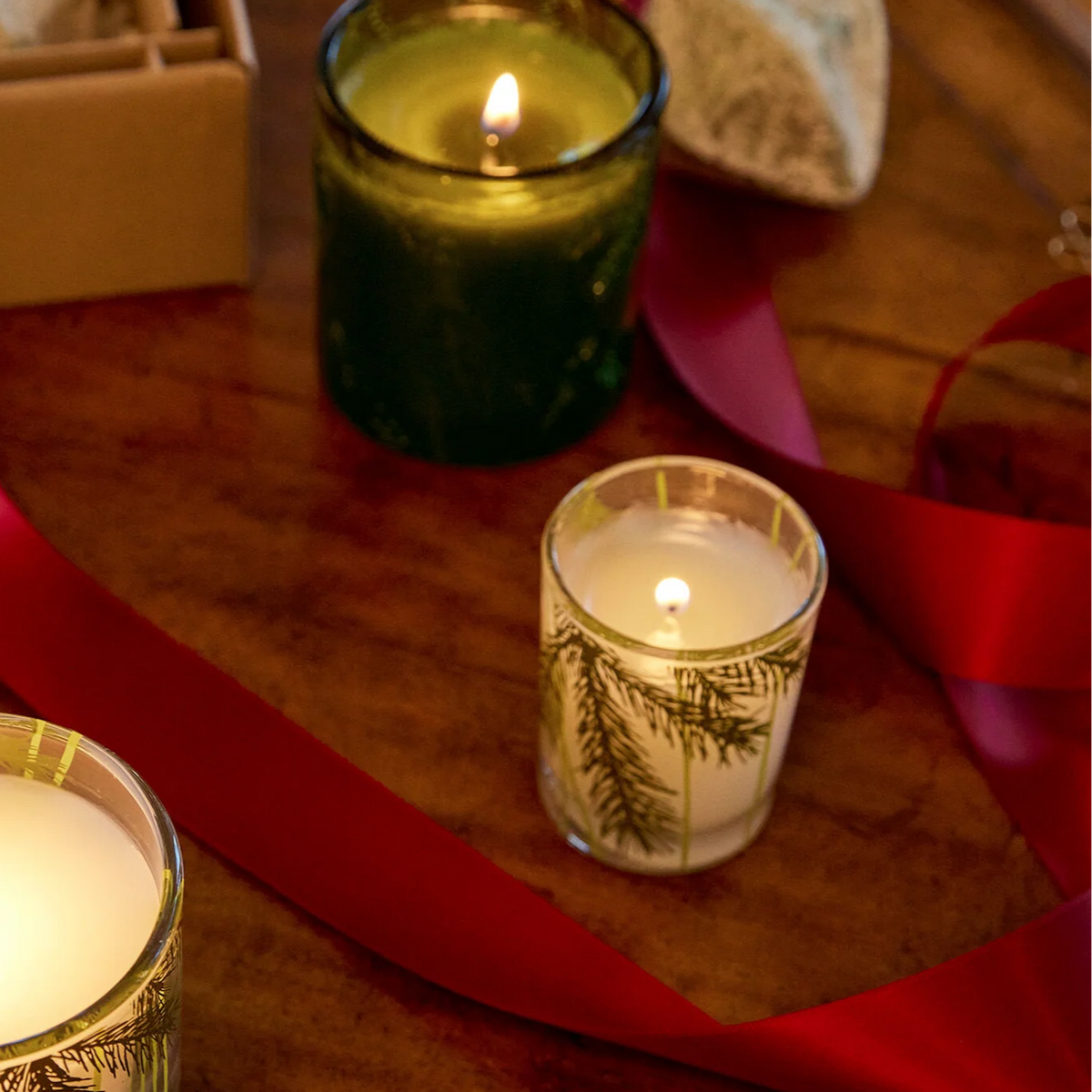 Mellow Monkey Thymes Frasier Fir pine needle votive candle with festive red ribbon on a wooden table