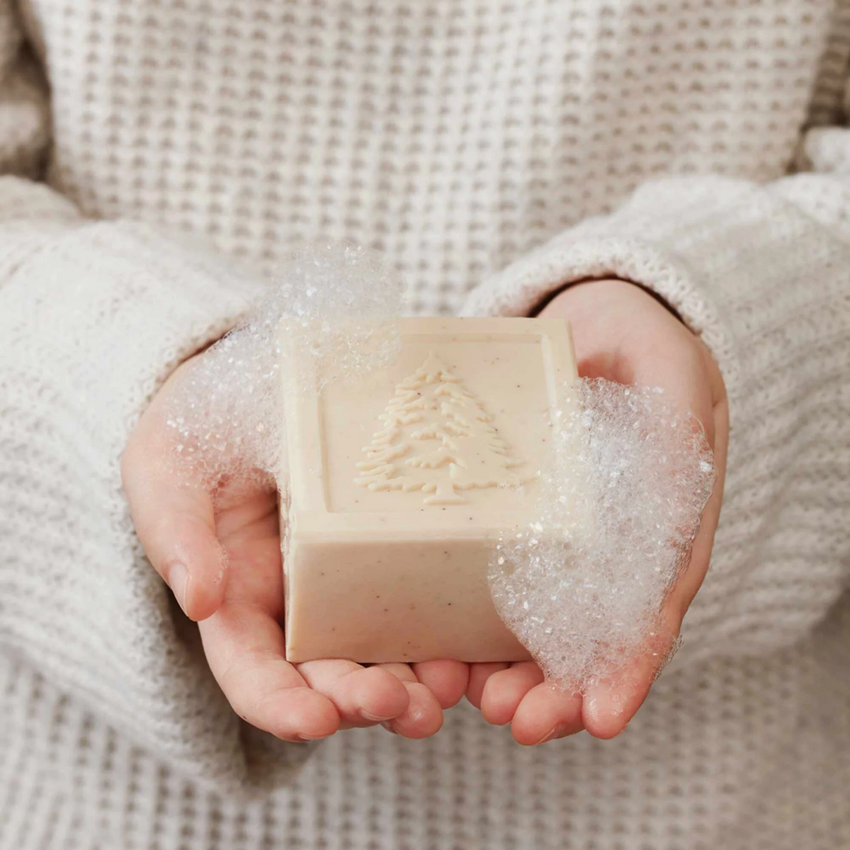Mellow Monkey Frasier Fir bar soap with embossed pine tree design held in hands with rich lather