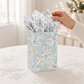 Mellow Monkey small frosted poinsettia gift bag with twisted paper handles and included tissue paper on a table.