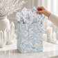 Mellow Monkey medium frosted poinsettia gift bag with blue and white floral print, twisted handles, and tissue paper.