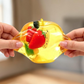Mellow Monkey transparent yellow apple squishy being stretched, filled with colorful miniature fruit pieces.