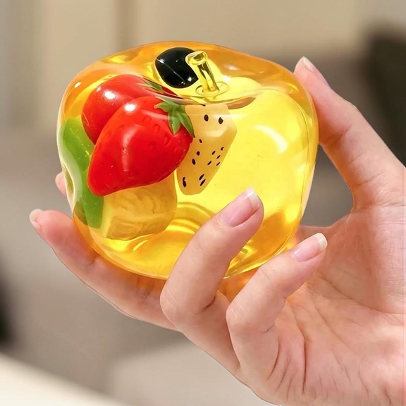Mellow Monkey transparent yellow apple squishy filled with colorful miniature fruit pieces held in a hand