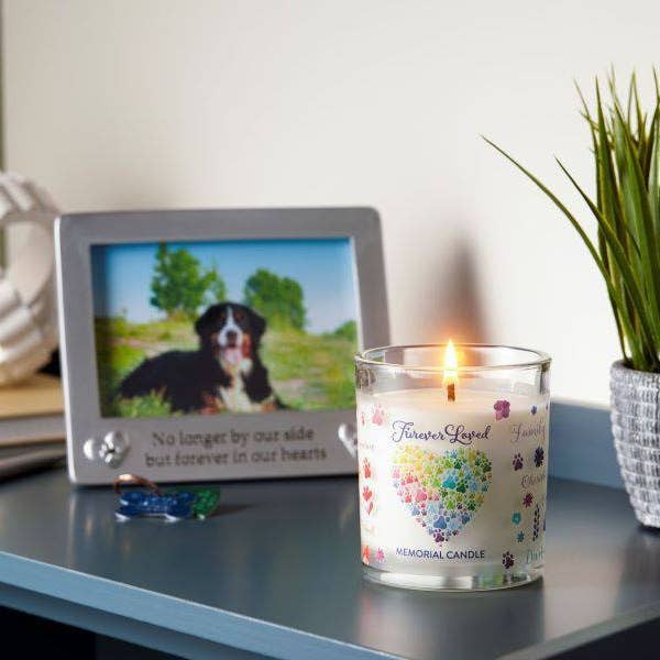 Mellow Monkey Furever Loved memorial pet house candle with colorful paw print design next to a dog photo frame