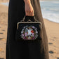 Mellow Monkey black linen kisslock bag featuring embroidered ghosts, snake, and floral wreath held at the beach.