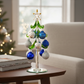 Mellow Monkey 8-inch glass Christmas tree with blue and silver ornaments and a star topper on a wooden table.