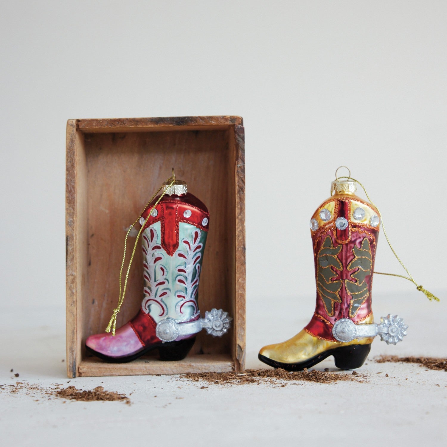 Mellow Monkey hand-painted glass cowboy boot ornaments with glitter and jewel accents in a rustic wooden crate