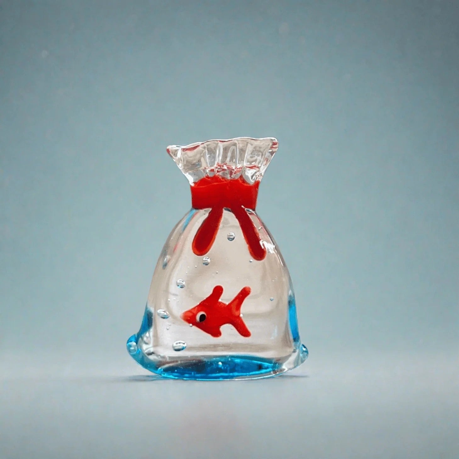 Mellow Monkey 1-inch miniature glass figurine featuring a small red fish inside a clear glass bag with blue base.