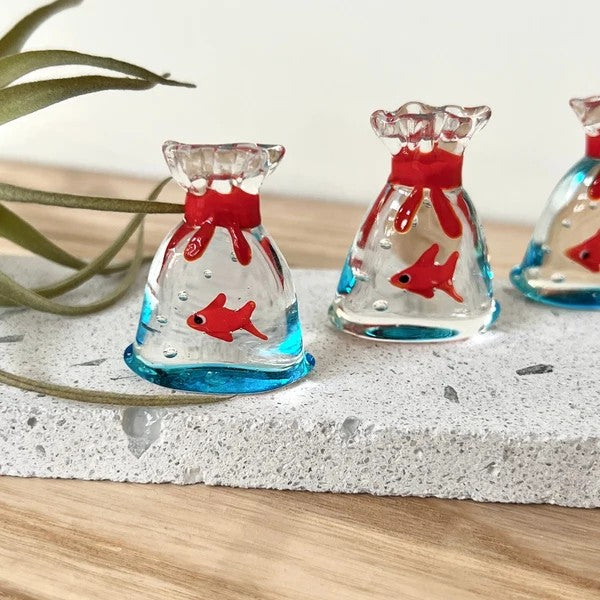 Mellow Monkey 1-inch miniature glass fish inside a clear glass bag with red tie detail on a stone display base