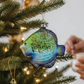 Mellow Monkey glass fish ornament in blue and green with gold glitter and beads hanging on a decorated Christmas tree