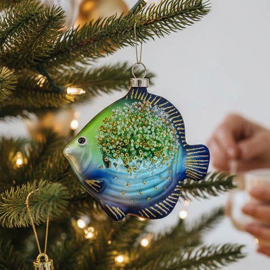 Mellow Monkey glass fish ornament in blue and green with gold glitter and beads hanging on a decorated Christmas tree