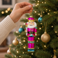 Mellow Monkey hand-blown glass nutcracker ornament in pink, turquoise, and gold hanging on a Christmas tree.