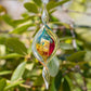 Mellow Monkey 9-inch hand-blown glass spiral ornament with vibrant red, blue, and gold leaf accents hanging outdoors.