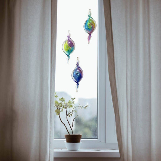Mellow Monkey hand-blown glass spiral ornaments in vibrant colors hanging in a window to catch the light.