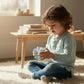 A child sitting on a rug playing with a Mellow Monkey 2-inch glitter-filled sensory squeeze cube toy.
