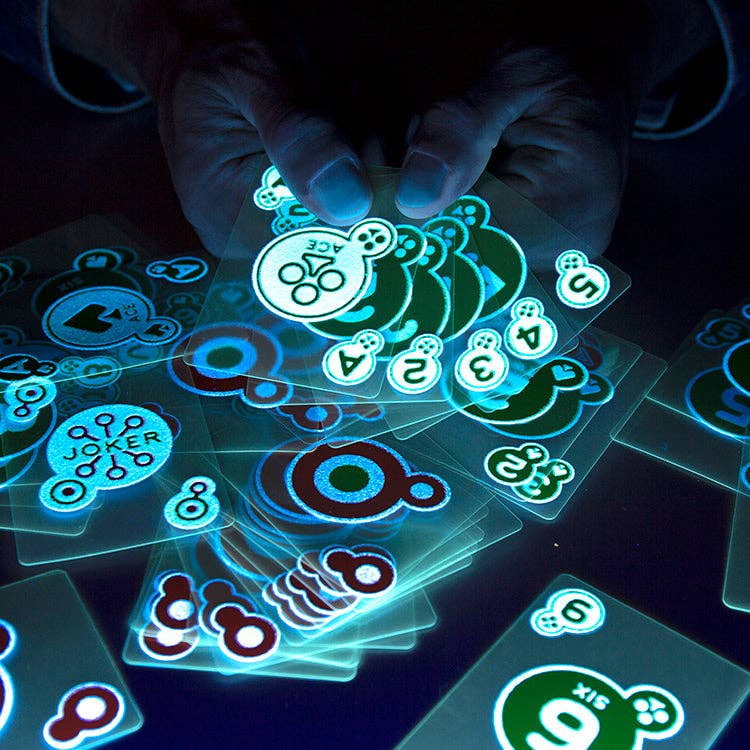 Mellow Monkey glow in the dark playing cards held in hands, emitting a bright blue light in a dark room.