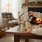 Mellow Monkey gold cast aluminum deer figurine displayed on a wooden table with holiday decor and a cozy fireplace.