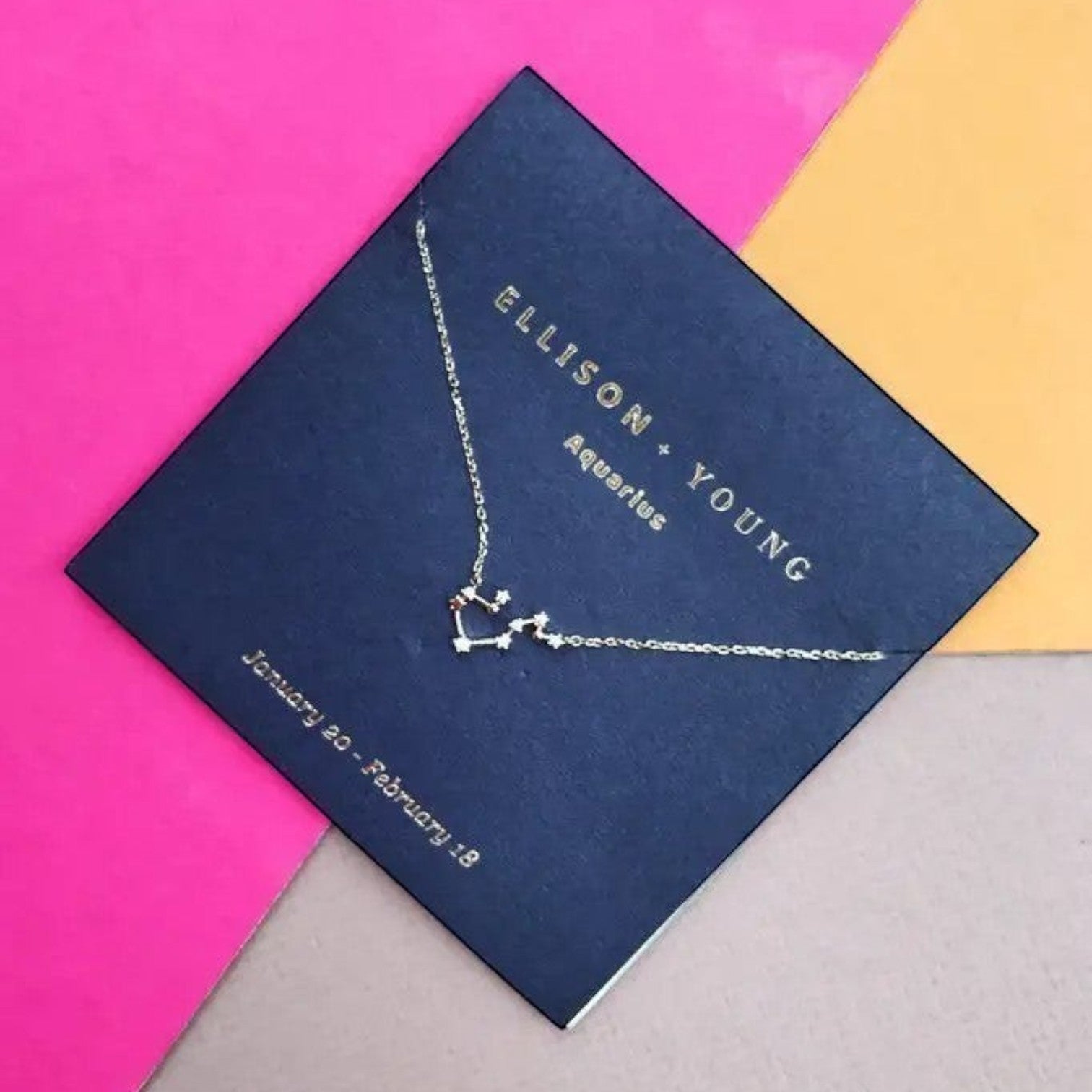 Mellow Monkey gold Aquarius zodiac constellation necklace with cubic zirconia accents on a navy card.