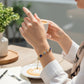 Mellow Monkey gold-tone bracelet featuring linked blue and clear crystals worn by a woman at a cafe table.