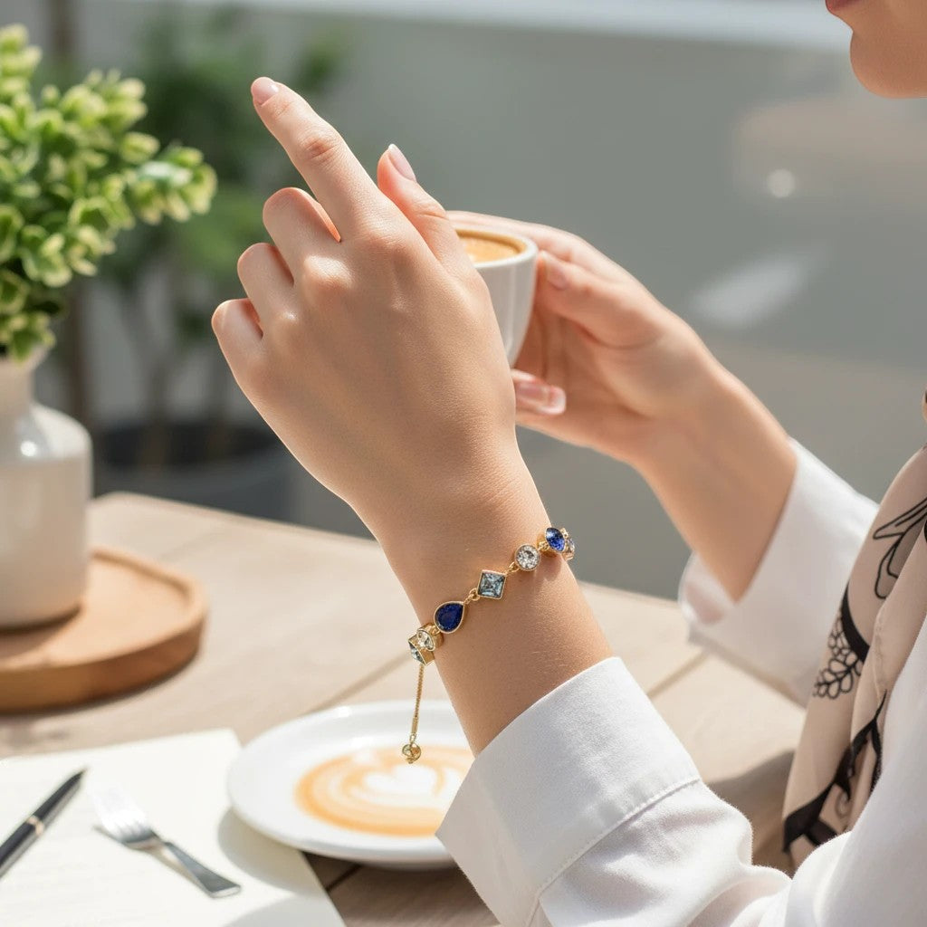 Mellow Monkey gold-tone bracelet featuring linked blue and clear crystals worn by a woman at a cafe table.
