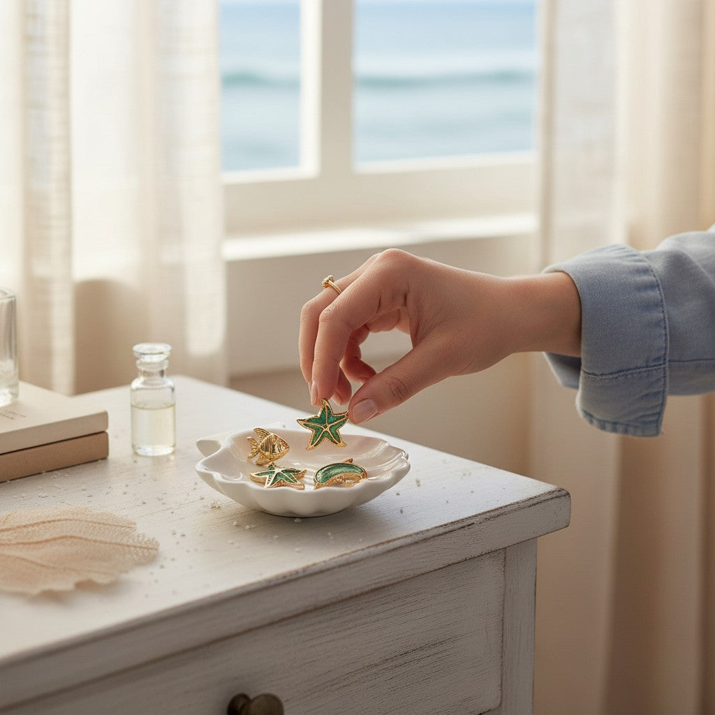Mellow Monkey gold-tone coastal earrings featuring dolphin and starfish designs in a white shell-shaped dish.