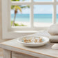 Mellow Monkey gold hoop earrings with coastal charms and pearls resting on a white dish by a beach view window.